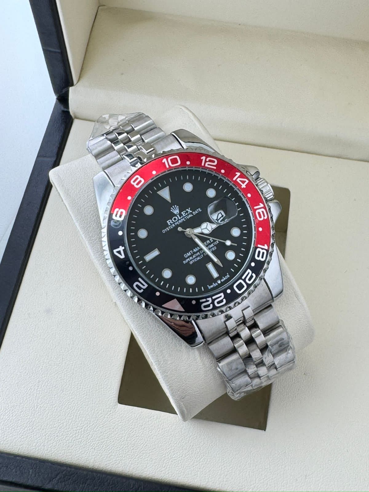 Rolex watch with black face and red bezel on a white cushion